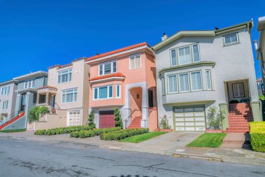 San Francisco 'da mavi gökyüzüne karşı üç katlı dış görünüşlü evler. Güneşli bir günde mahalle caddesinden manzaralı pencereli, garajlı ve açık merdivenli evler..
