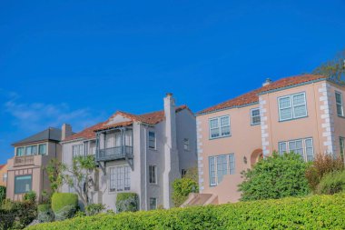 Güneşli bir günde mavi gökyüzü arka planına sahip San Francisco California evleri. Büyüleyici evlerin önünde yemyeşil yapraklar ve ağaçlar görülebilir..