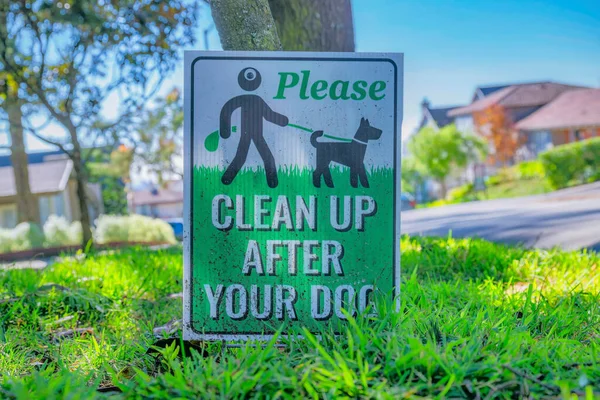 Please Clean Up After Your Dog sign at a neighborhood in San Francisco. Close up view of a pet signage against tree, road, houses and blue sky on a sunny day.