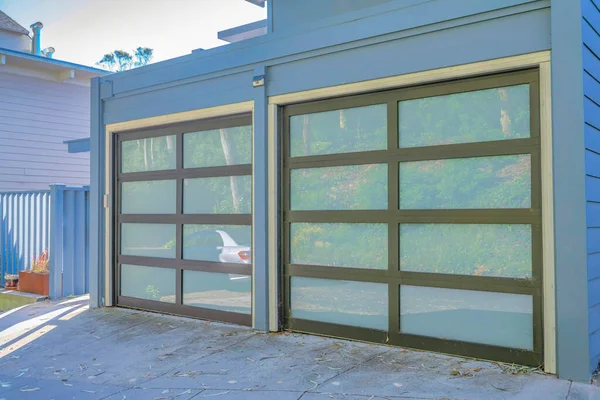 Garage doors with glass panes at the facade of home in San Francisco California. The glass doors reflects a car parked on the neighorhood road on this sunny day.