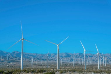 Yenilenebilir yeşil enerji üreten üç keskin bıçaklı yel değirmenleri. Güneşli bir günde güneş ışığıyla aydınlatılan engin kuru tarlalarda yükselen beyaz rüzgar pompaları..