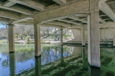 San Antonio Teksas 'taki River Walk köprüsünün altındaki kanal manzarası. Turistler için yol ve binalar güneşli arka planda görülebilir..