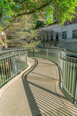 San Antonio Teksas 'taki River Walk' taki pitoresk kanalın üzerindeki patika köprü. Asfalt yol bu güneşli günde sakin sulara ve binalara bakıyor..