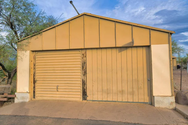 Tucson, Arizona- Detached garage exterior with painted cream two garage doors and peak. There is a garage door with horizontal panel on the left beside the wider garage door with vertical panels.