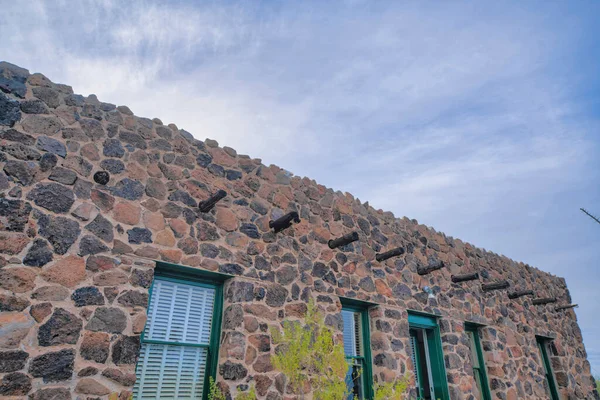 Stone house with green window frames and wooden vigas- Tucson, Arizona. Exterior of a stone house in a low angle view with plants at the front and sky background.