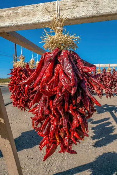 Hanging chili peppers for sale on the side of road in Tucson, Arizona. Bright red strings of chili peppers hanging on a wood stand against the blue sky.