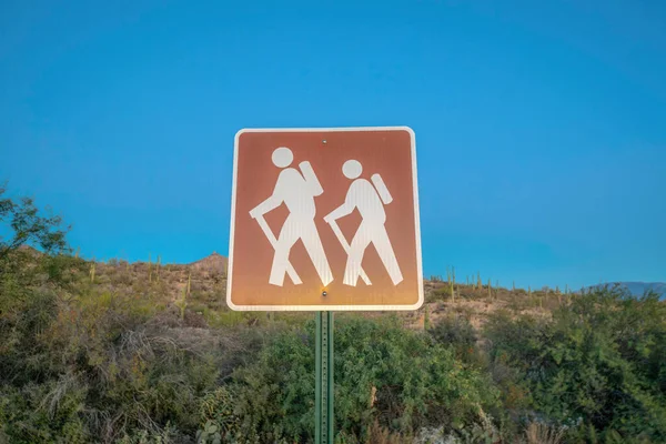 Hiking trail sign post against the slope and blue sky at Sabino Canyon State Park- Tucson, Arizona. Sign post symbol with two hikers illustration.