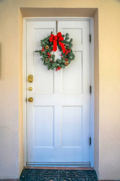 Downtown Tucson, Arizona- White front door with decorative wreath. Front door exterior with doormat, three gold doorknobs, and painted cream walls.