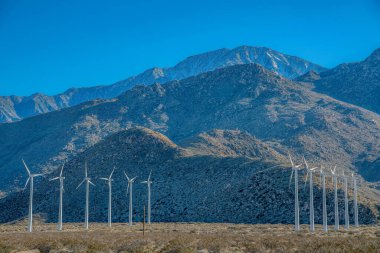Palm Springs, California. Çöldeki yel değirmenleri. Rüzgâr türbinleri arka plandaki kuru dağ yamaçlarına karşı sırayla geliyor..