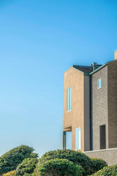 La Jolla, California- Residential house building with bricks and painted beige wall. There are green bushes outside the fenced house against the clear sky background.