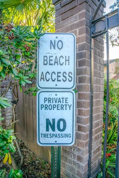La Jolla, California-Two signs on a post with No Beach Access, Private Property, and No Tresspassing. Signages on a post outside a gate with bricks pillar and plants near the wall.
