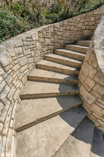 San Antonio, Texas- Concrete steps of an outdoor staircase with stone walls. Stairs in the middle of stone walls and a view of plants at the top.