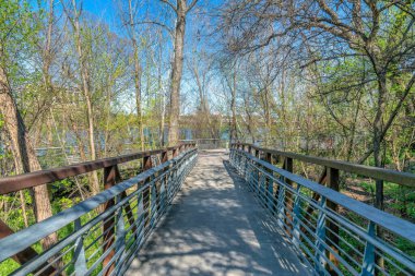 Austin, Teksas. Nehrin kıyısında, ağaçların ortasında. Bisiklet yolu ve yaya yolu su ve mavi gökyüzü manzarasına karşı beton kaldırımlı..