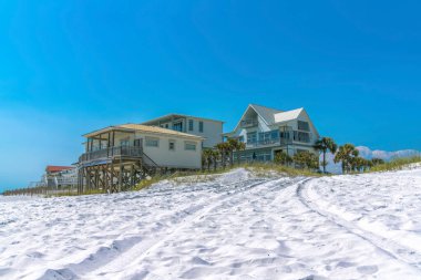 Florida, Destin 'de beyaz bir kumsalda yazlık evler. Açık mavi arka planda sütunları ve terası olan sahil evleri var..
