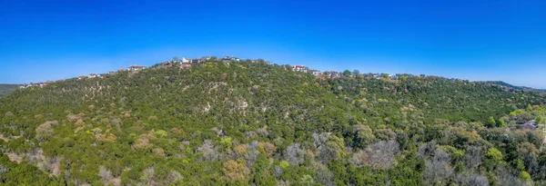 Austin, Texas- Panoramic view of a green mountain slope with residential buildings at the top. View of a rich neighborhood on top of a mountain against the blue sky background.