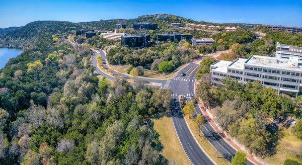 Austin, Texas- Aerial view of business buildings in the middle of forest near the river. Business area with paved roads near the green mountain slopes.