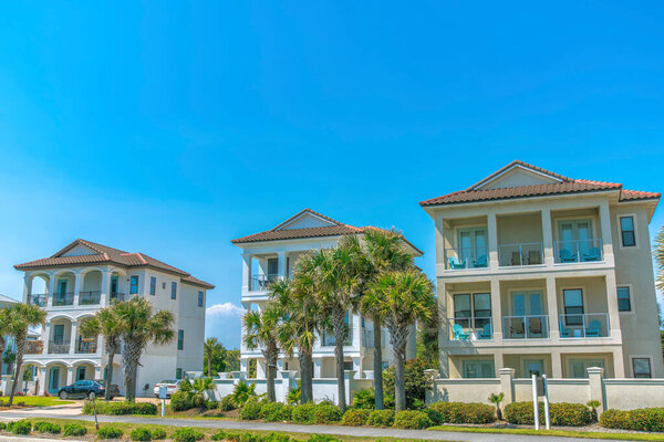 Дестин, Флорида - фасад огороженных трехэтажных пляжных домов. Рядом с пальмами и кустами у стены забора есть пешеходная дорожка..
