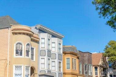 San Francisco, California 'da açık mavi gökyüzüne karşı farklı yapılara sahip evler. Çevrede duvarları, pencereleri, kiremitleri ve ağaçların manzarası olan evler var..