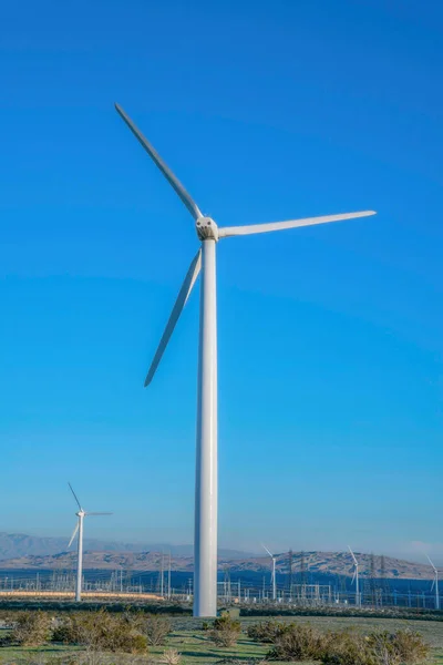 Tubular steel wind turbine tower in a desert at California. Close-up of a windmill tower with other wind turbines at the back against the mountains and sky at the back.