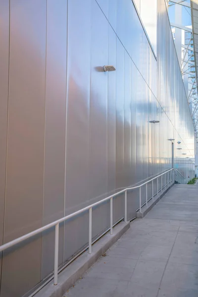 Footpath with handrails near the metal wall of a building at Phoenix, Arizona. Concrete pavement with handrails near the cream metal walls on the left.