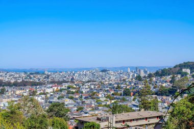 San Francisco, California 'ya bakan şehir manzarası. Dağların yakınındaki yoğun binaların ve açık mavi gökyüzünün arkasındaki körfezin görüntüsü.