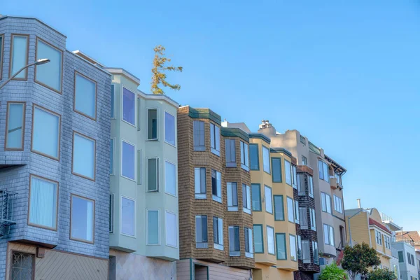 Small apartment buildings with different wall sidings and window structures in San Francisco, CA. Row of apartment buildings with traditional designs against the clear sky background.