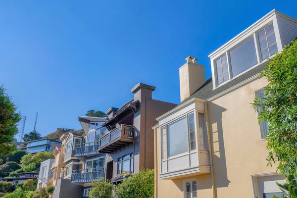 Row of suburban houses near a slope with two towers at the back in San Francisco, California. There is a beige house at the front with bay window along with the houses with balconies.