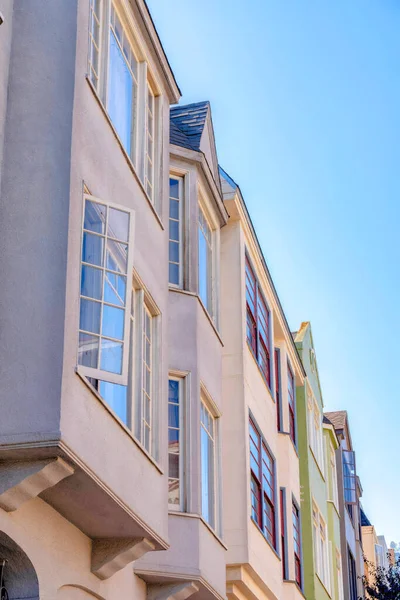 Casement windows of houses against the sky in San Francisco, California. Side view of houses exterior from below with painted walls.
