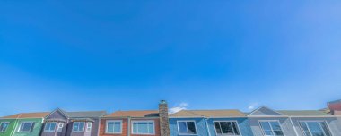 San Francisco, Kaliforniya 'da mavi gökyüzüne karşı alçak açılı evlerin zirveleri. Resimli pencereli banliyö evleri dizisi.