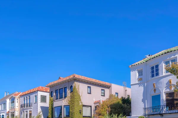 Mediterranean houses against the sky at San Francisco, California. Side view of middle class neighborhood with tall trees outdoors and houses with railings and clay tile roofs.