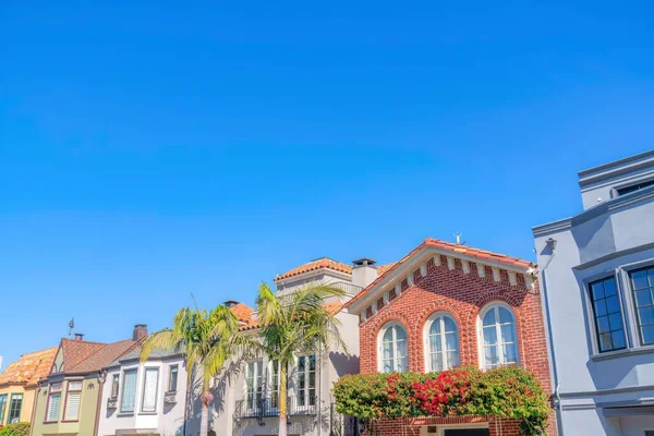 Exterior of houses with bricks and painted stucco walls in San Francisco, CA. There is a brick house with arched windows and crawling plants in the middle of painted houses with trees at the front.