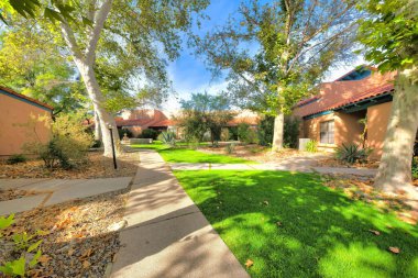 Tucson, Arizona 'da bir apartman dairesinde evlerin ortasındaki yol. Evlerin girişlerine giden yol yeşil çimenler ve ağaçlarla dolu..