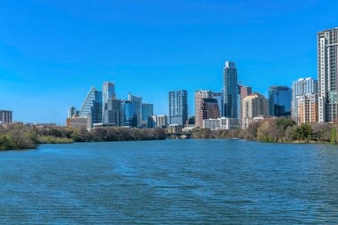 Austin Texas 'ın modern lüks daireleri ve Colorado Nehri' nin manzaralı silueti. Sakin su manzaralı panoramik şehir manzarası ve mavi gökyüzüne karşı pahalı konut binaları.