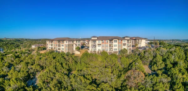 Austin, Texas- Apartment complex near the tree forest. There are trees on the slope at the front and a background of clear blue sky background.