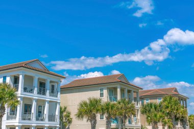 Destin, Florida. Önünde balkonları ve palmiye ağaçları olan yazlık evler. Gökyüzü arka planına karşı üç katlı evler cephesi.