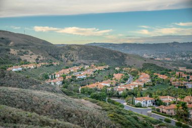San Clemente, California 'daki yürüyüş parkurundan zengin bir mahalle manzarası. Önünde yeşil bir dağ yamacı var, yerleşim alanı ve arka planda gökyüzü manzarası var..