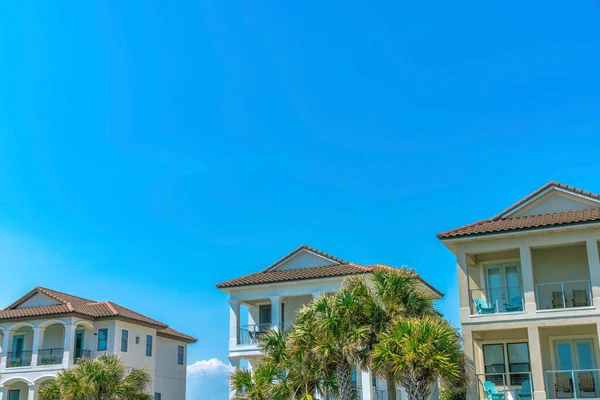Destin, Florida. Balkonların önünde palmiye ağaçları ve koltukları olan plaj evleri. Mavi arka planda balkonları olan büyük yazlık evler..