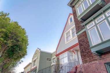 San Francisco, California civarındaki evler. Ortasında bir ev var. Ön tarafında parmaklıklar var. Sağında tahta kiremitler ve resim camları var..
