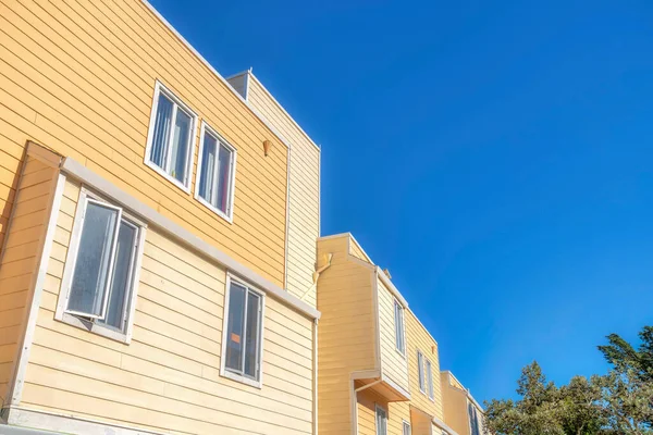 Low angle view of an apartment building with casement windows and wood lap siding in San Francisco. Apartment building exterior with yellow wood siding and glass casement windows against the sky.