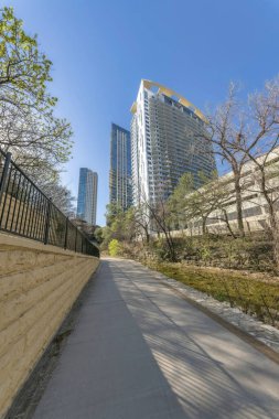 Mavi gökyüzüne karşı binaların manzarası olan bir duvar boyunca uzanan Paved geçidi. Güneşli bir günde patikası ve apartmanı olan Austin Texas şehir merkezinin manzarası..