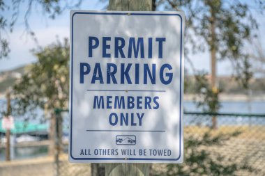 Otopark görevlileri sadece Teksas 'taki Austin Gölü' nün bulanık manzarasına karşı imza atar. Bilgi işareti üyesi olmayanlara park yasağı ve araçların çekilebileceği uyarısı.