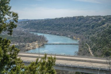 Colorado Nehri 'nin Austin Barajı' ndan beton köprü manzarası. Güneşli bir günde ağaçların ve gökyüzünün yemyeşil yaprakları arasında suyun ve yolun havadan manzarası..