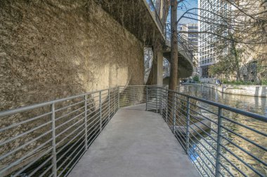 San Antonio River Walk, Teksas 'taki kanal manzaralı yürüyüş yolu. Ziyaretçiler ve turistler etrafı gezerken suyun üzerinde parmaklıklar olan beton bir patika..
