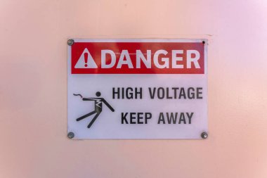 Tehlike Yüksek Voltaj Uzak Kal, San Antonio, Teksas tabelasına yakın çekim. Arka plandaki boyalı şeftali duvarına işaret asılmış..