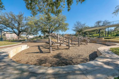 Austin, Teksas. Waterloo Park 'taki bir oyun parkındaki ahşap kütükler. Çocuk parkının arkasında, arkasında korkuluklar ve ağaçlar olan yüksek bir patika var..