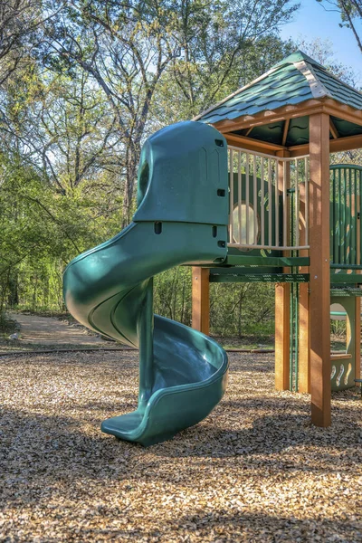 Austin, Texas- Spiral slides on a community playground. View of a slide for kids against the view of a trail in the middle of a forest at the background.