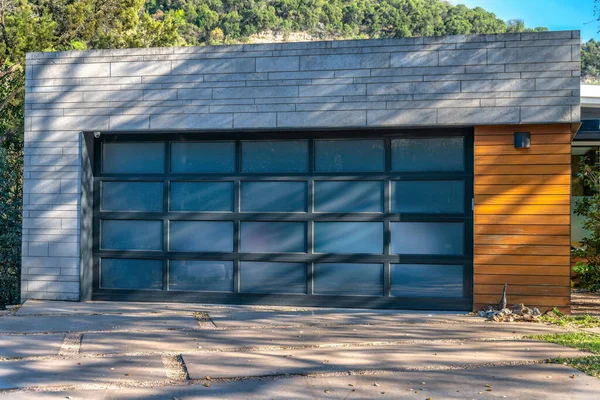 Modern detached garage exterior with frosted glass panels on garage door- Lake Austin, Austin, Texas. Garage exterior with gray concrete wall and wood cladding.
