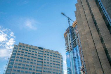Austin, Teksas. İki binanın alçak açılı ve biri inşaat halinde. İnşaatın önündeki cam binanın önünde bir vinç ve yan taraftaki iki binanın görüntüsü var..
