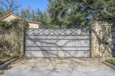 San Antonio, Teksas. Taş sütun duvarlarına metal levha ile demir kapı yazmış. Kapalı bir evin garaj yolu, duvarlarında asmalar, evin manzarası ve arkada ağaçlar var..