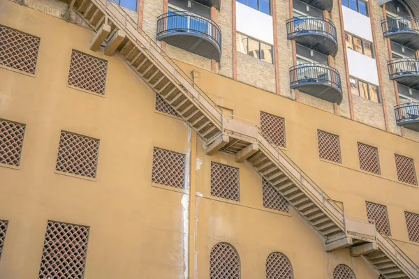 Staircase outside a building with concrete screen windows- San Antonio, Texas. Building with bricks wall and balconies above the yellow wall.